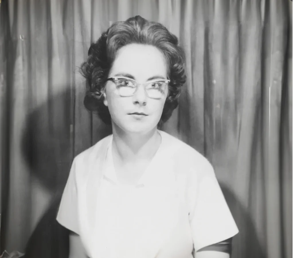 The same black-and-white portrait, widened by AI to show more of the curtain behind her and her shoulders and blouse below.